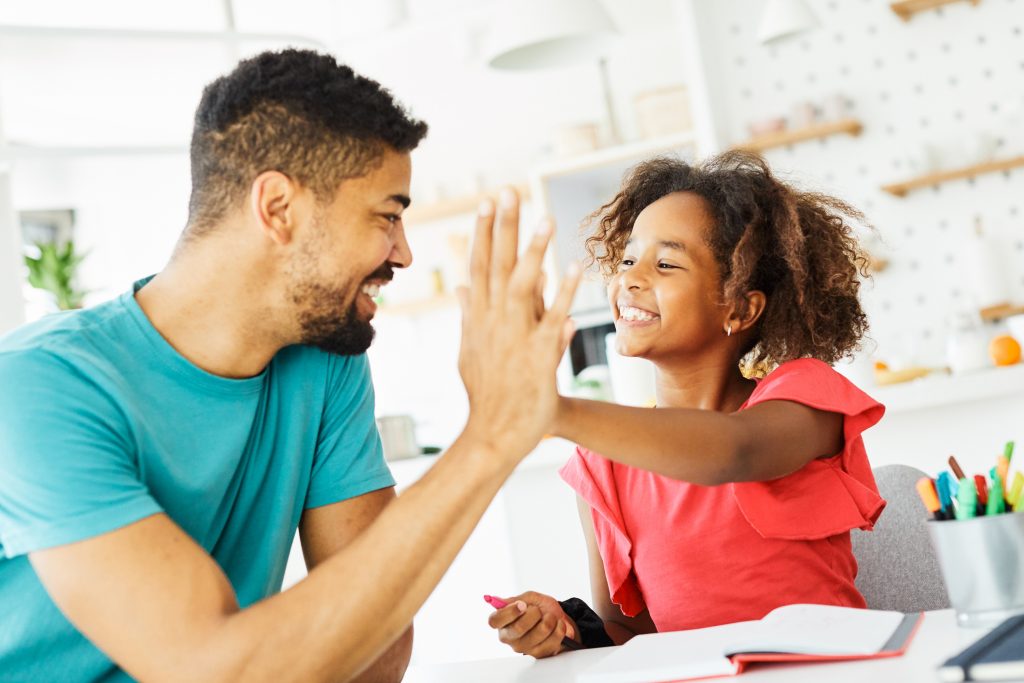father teaching daughter and helping with homework at home, daughter giving high five to father