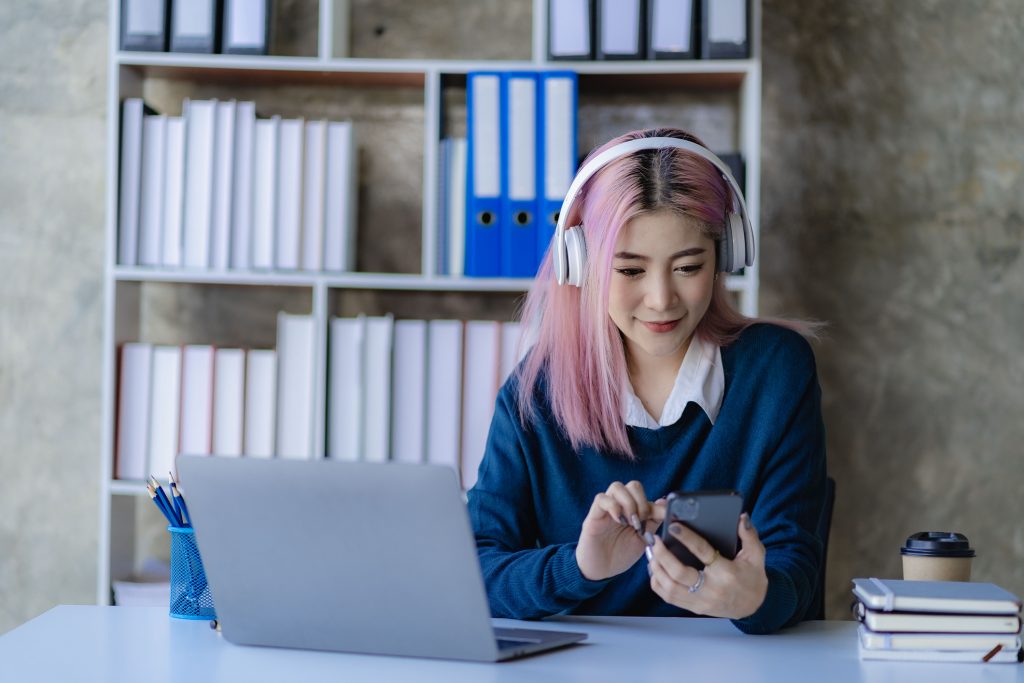 Asian female college students wearing headphones are using smartphones and laptops to surf the internet in preparation for university.