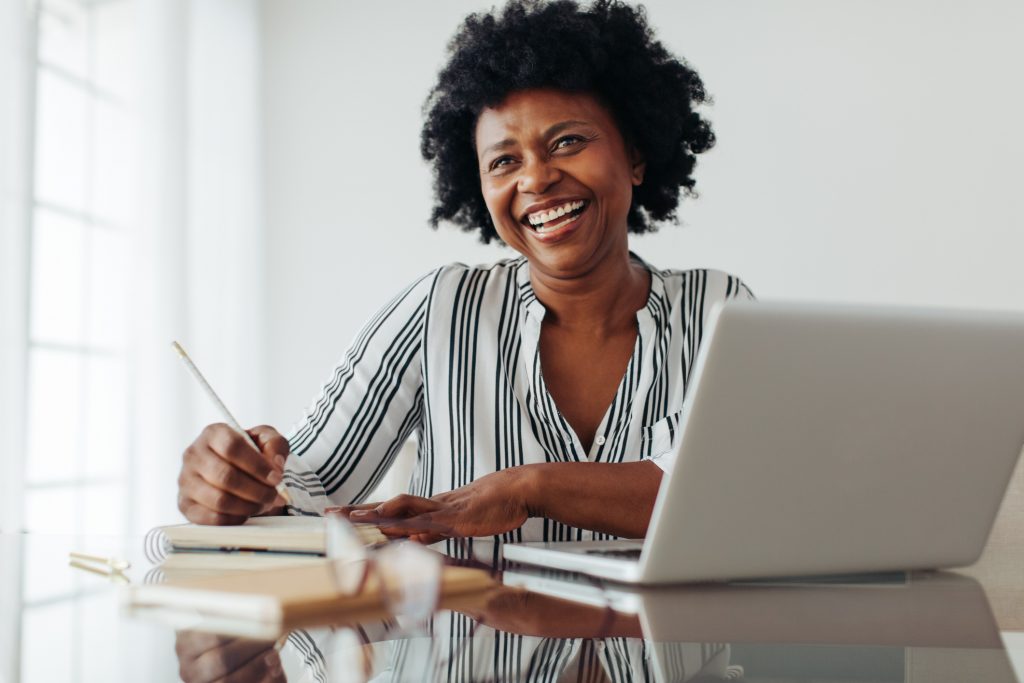 Portrait of a smiling woman sitting at table with laptop and dairy. Woman smiling at camera while working from home office.